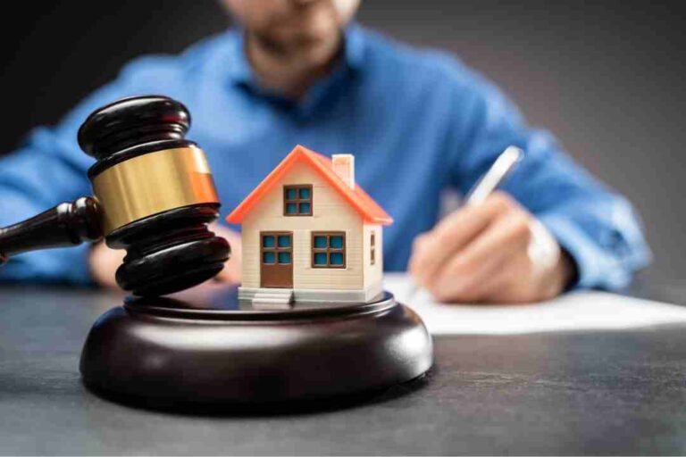 Gavel and a model house in foreground with a person writing in the background.